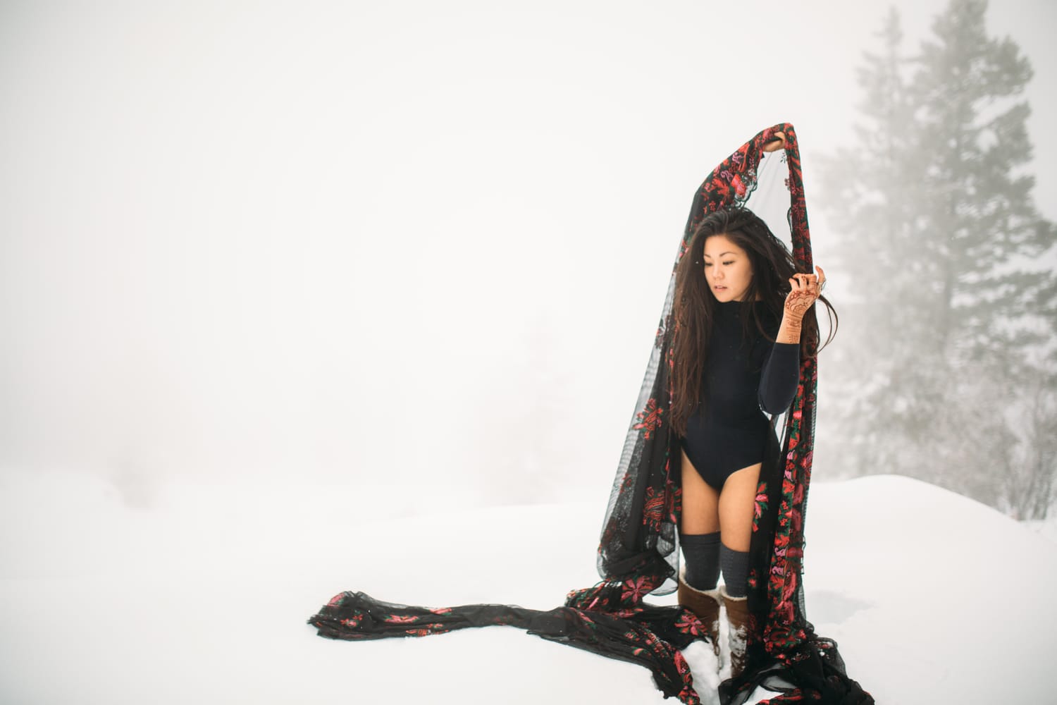 Sarah in the Snow portraits story frame 1: A winter portrait session for Sarah in Kelowna, with snow, black wardrobe, sheer floral fabric, whiteout atmosphere and bold movement in a cold landscape.