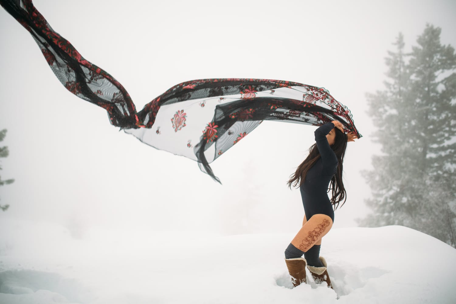 Sarah in the Snow portraits story frame 2: A winter portrait session for Sarah in Kelowna, with snow, black wardrobe, sheer floral fabric, whiteout atmosphere and bold movement in a cold landscape.