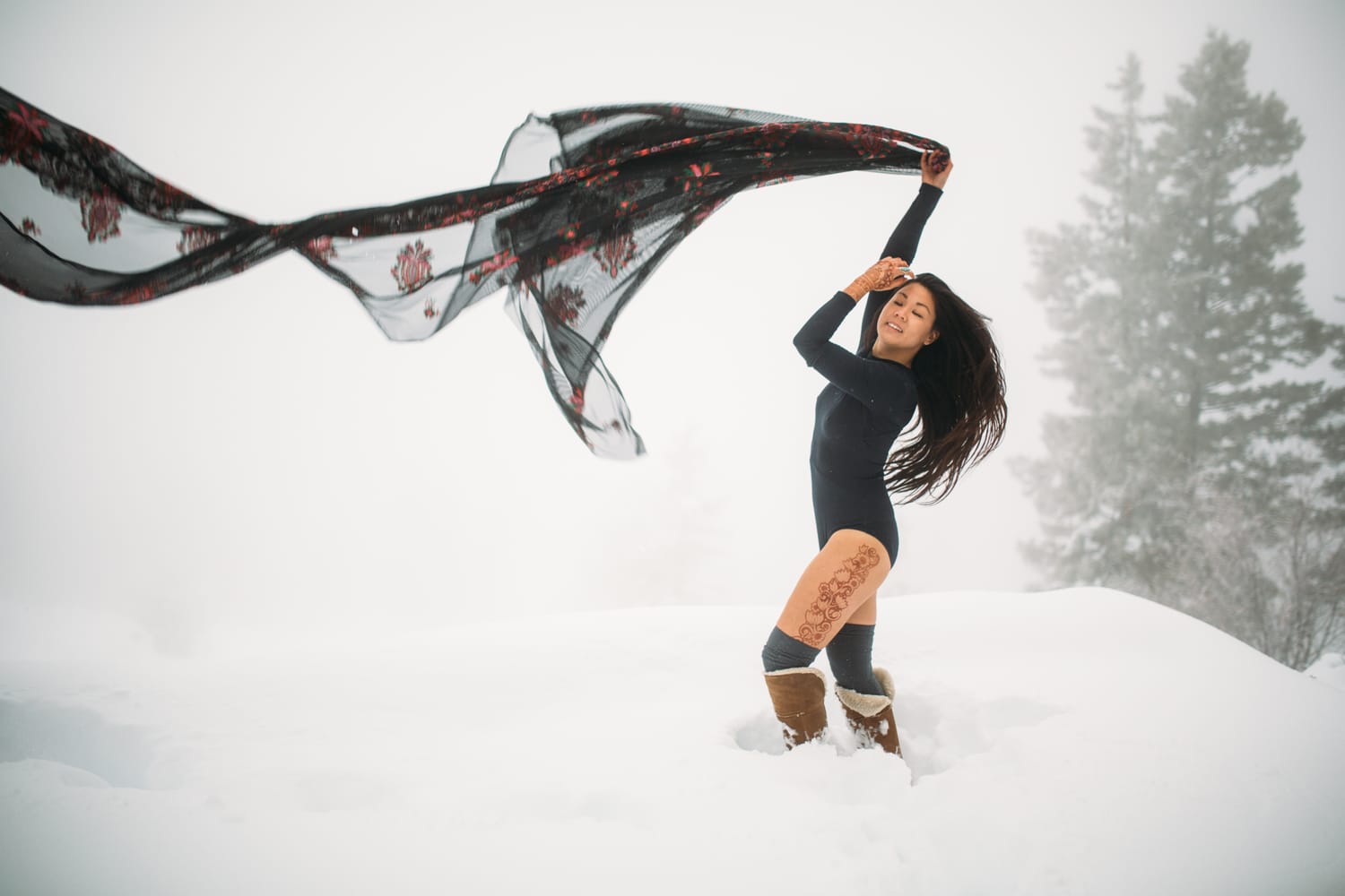 Sarah in the Snow portraits story frame 3: A winter portrait session for Sarah in Kelowna, with snow, black wardrobe, sheer floral fabric, whiteout atmosphere and bold movement in a cold landscape.