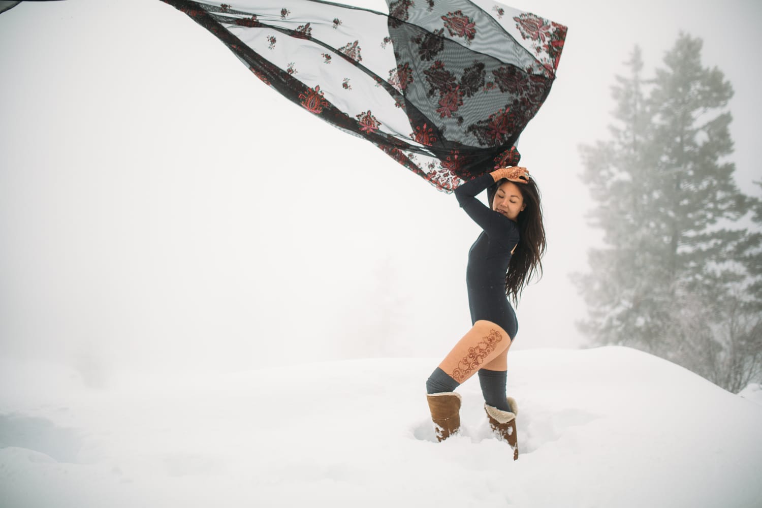 Sarah in the Snow portraits story frame 4: A winter portrait session for Sarah in Kelowna, with snow, black wardrobe, sheer floral fabric, whiteout atmosphere and bold movement in a cold landscape.
