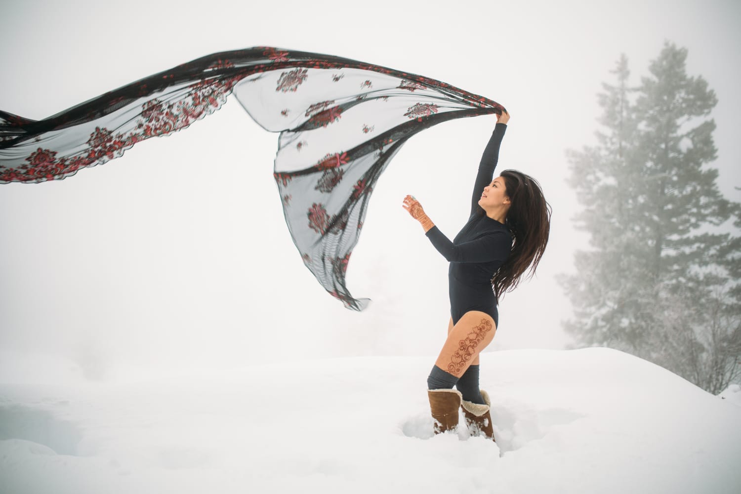Sarah in the Snow portraits story frame 5: A winter portrait session for Sarah in Kelowna, with snow, black wardrobe, sheer floral fabric, whiteout atmosphere and bold movement in a cold landscape.