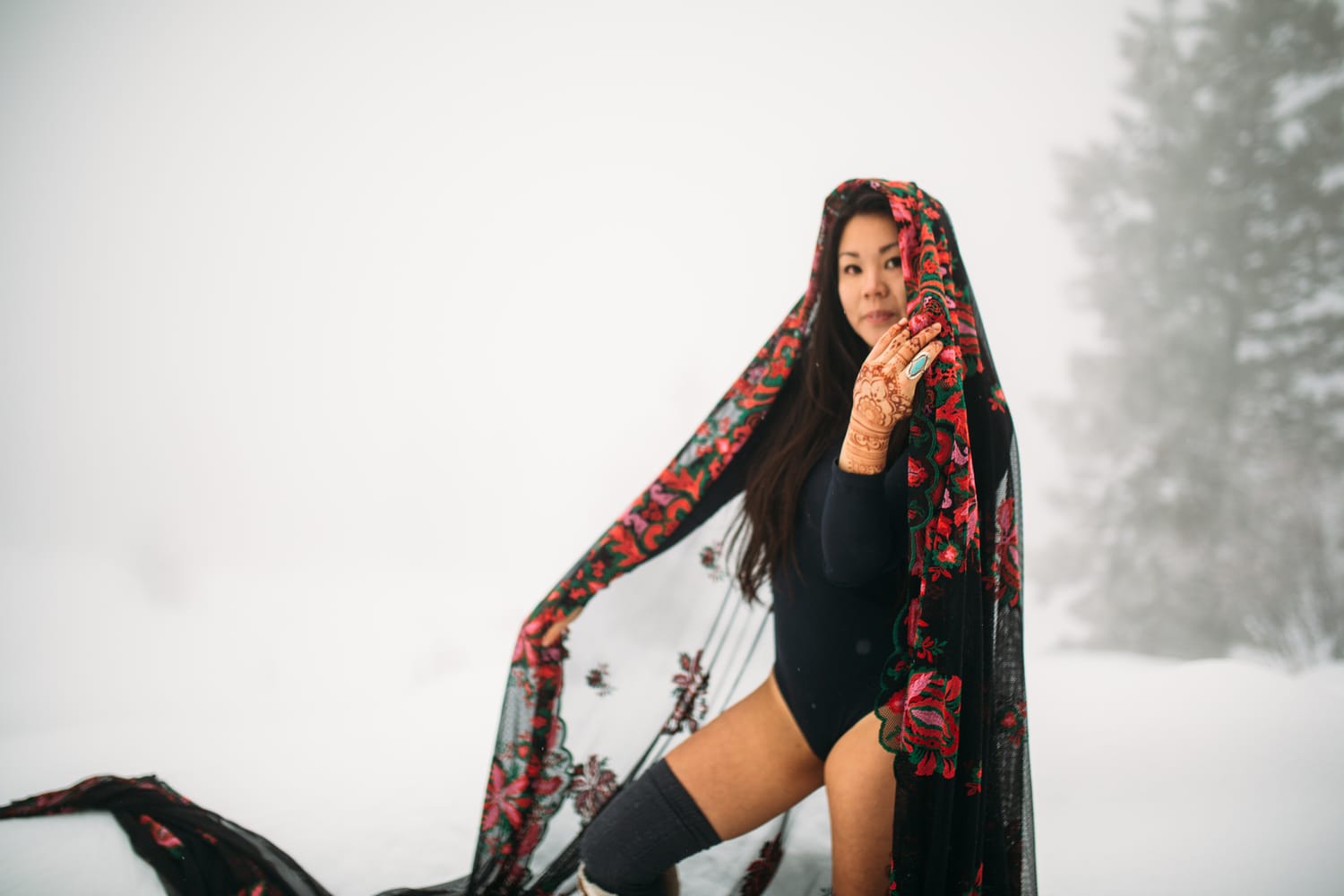 Sarah in the Snow portraits story frame 8: A winter portrait session for Sarah in Kelowna, with snow, black wardrobe, sheer floral fabric, whiteout atmosphere and bold movement in a cold landscape.