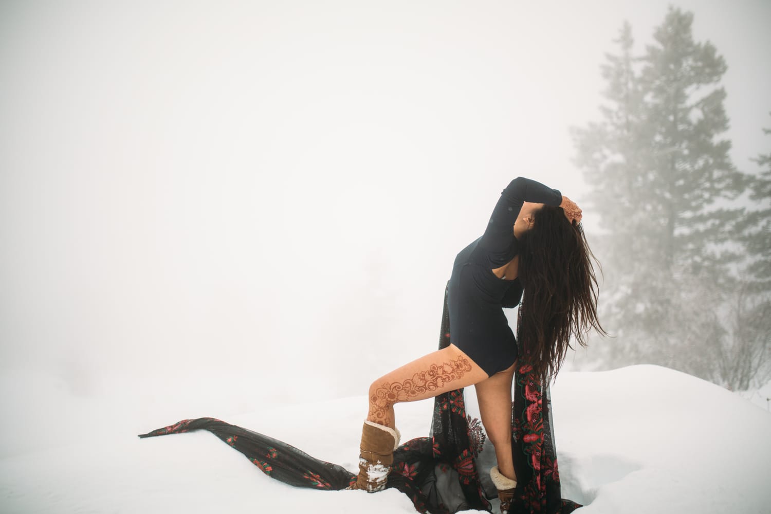 Sarah in the Snow portraits story frame 9: A winter portrait session for Sarah in Kelowna, with snow, black wardrobe, sheer floral fabric, whiteout atmosphere and bold movement in a cold landscape.