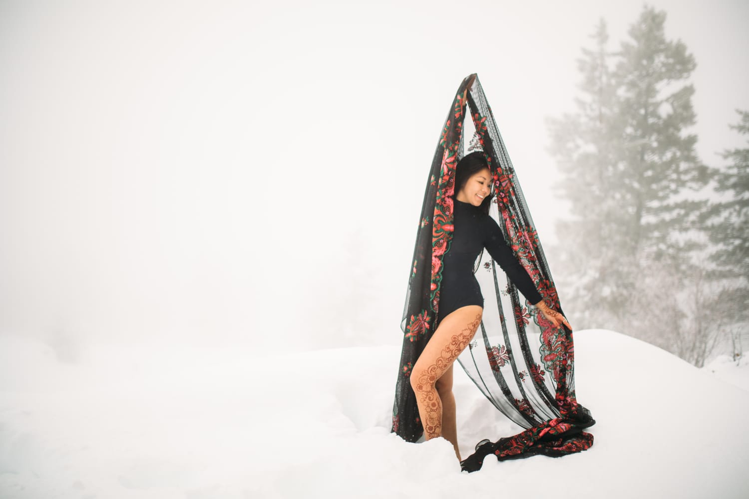 Sarah in the Snow portraits story frame 16: A winter portrait session for Sarah in Kelowna, with snow, black wardrobe, sheer floral fabric, whiteout atmosphere and bold movement in a cold landscape.