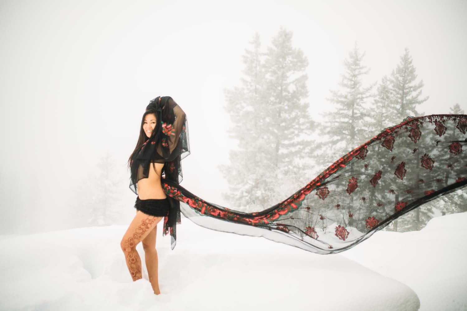 Sarah in the Snow portraits story frame 17: A winter portrait session for Sarah in Kelowna, with snow, black wardrobe, sheer floral fabric, whiteout atmosphere and bold movement in a cold landscape.