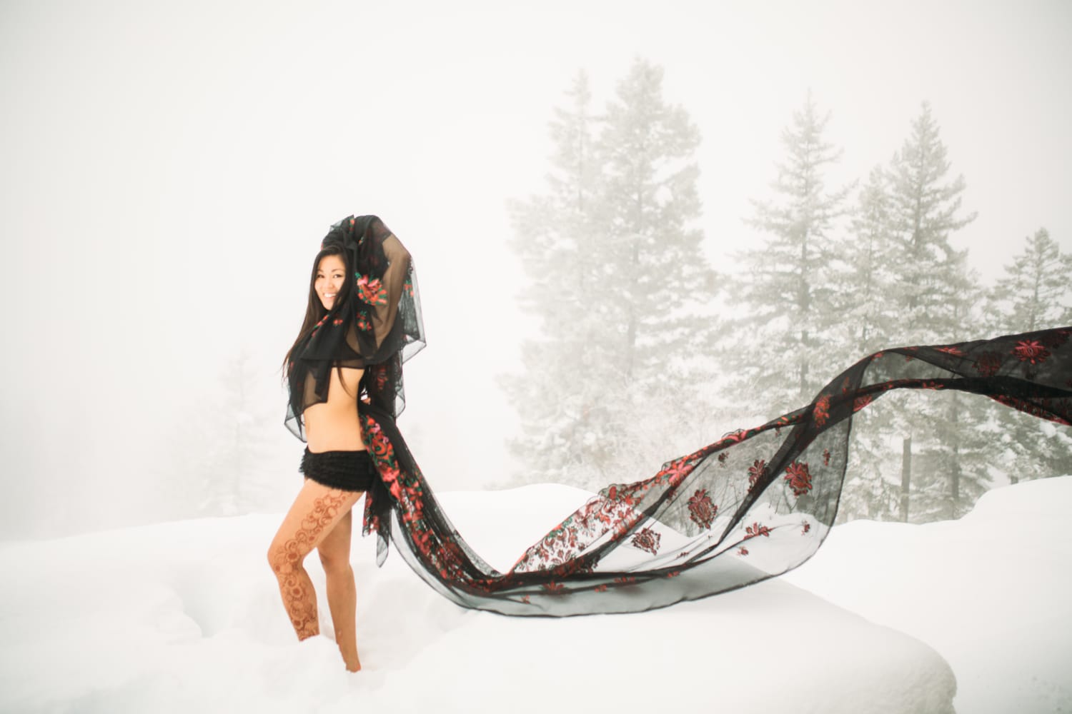 Sarah in the Snow portraits story frame 18: A winter portrait session for Sarah in Kelowna, with snow, black wardrobe, sheer floral fabric, whiteout atmosphere and bold movement in a cold landscape.