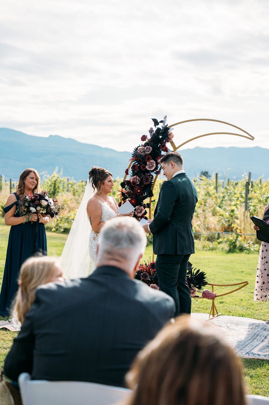 Taryn and Kai weddings story frame 19: An Okanagan vineyard wedding with ceremony, veil, guests, family, makeup by Guisachan Esthetics, and laughter woven through the altar moments..