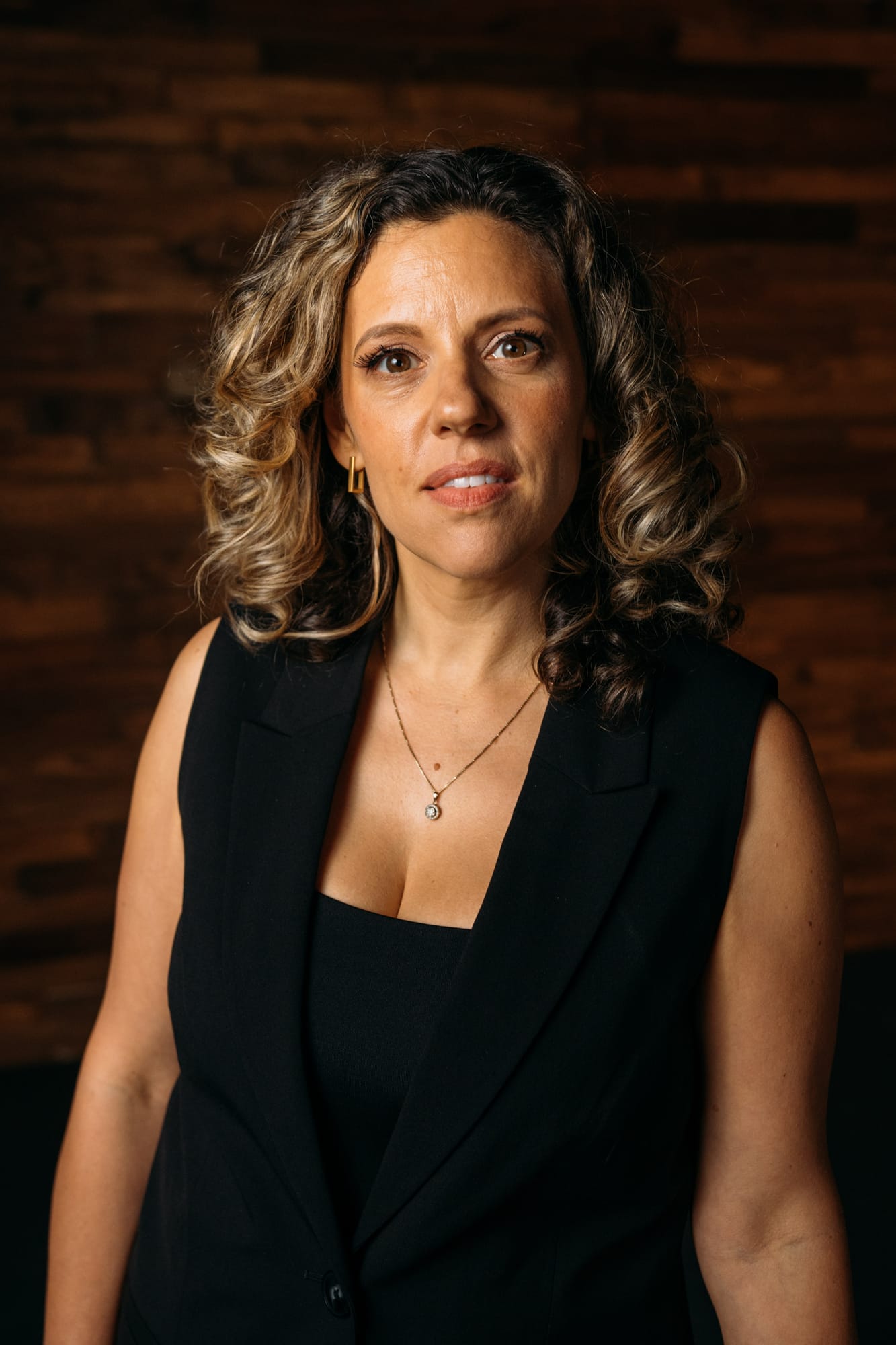 Trisha Miltimore corporate story frame 4: Personal-brand portraits for Trisha Miltimore in Kelowna, moving from clean business profile images into darker wood-wall portraits with black wardrobe and confident brand range..