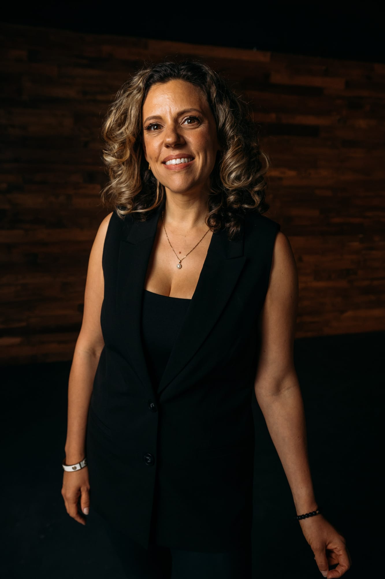 Trisha Miltimore corporate story frame 5: Personal-brand portraits for Trisha Miltimore in Kelowna, moving from clean business profile images into darker wood-wall portraits with black wardrobe and confident brand range..