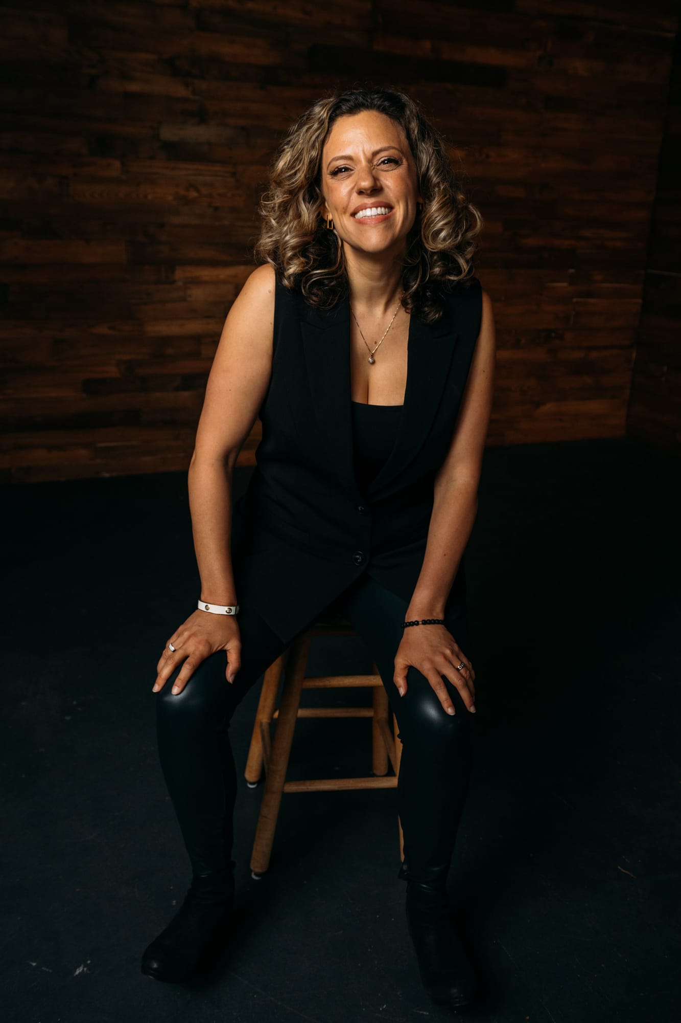 Trisha Miltimore corporate story frame 8: Personal-brand portraits for Trisha Miltimore in Kelowna, moving from clean business profile images into darker wood-wall portraits with black wardrobe and confident brand range..