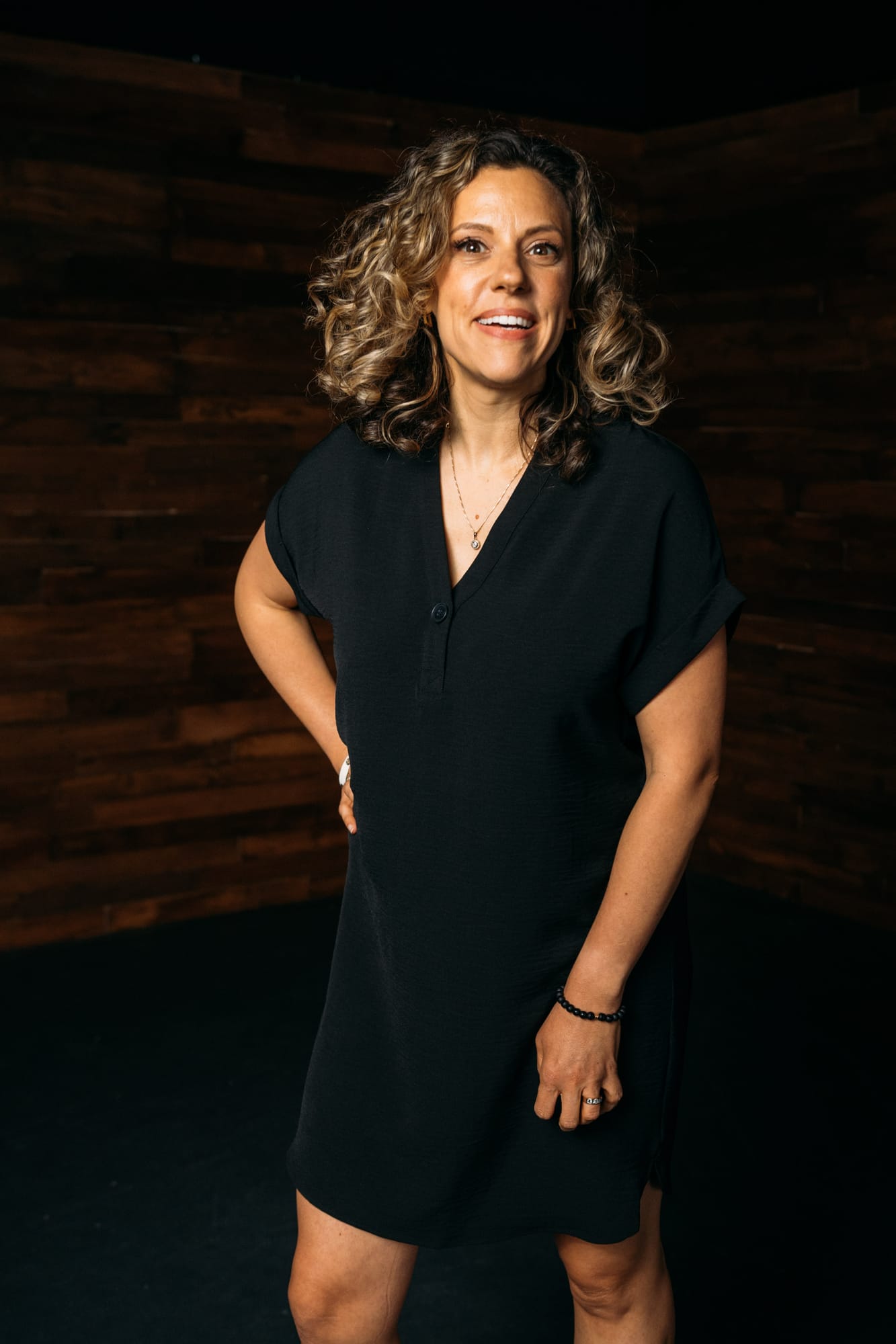 Trisha Miltimore corporate story frame 10: Personal-brand portraits for Trisha Miltimore in Kelowna, moving from clean business profile images into darker wood-wall portraits with black wardrobe and confident brand range..