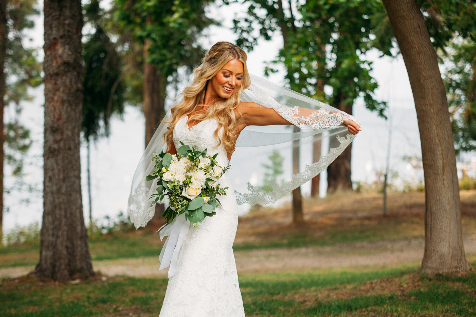 Bride holding her bouquet beside trees and water